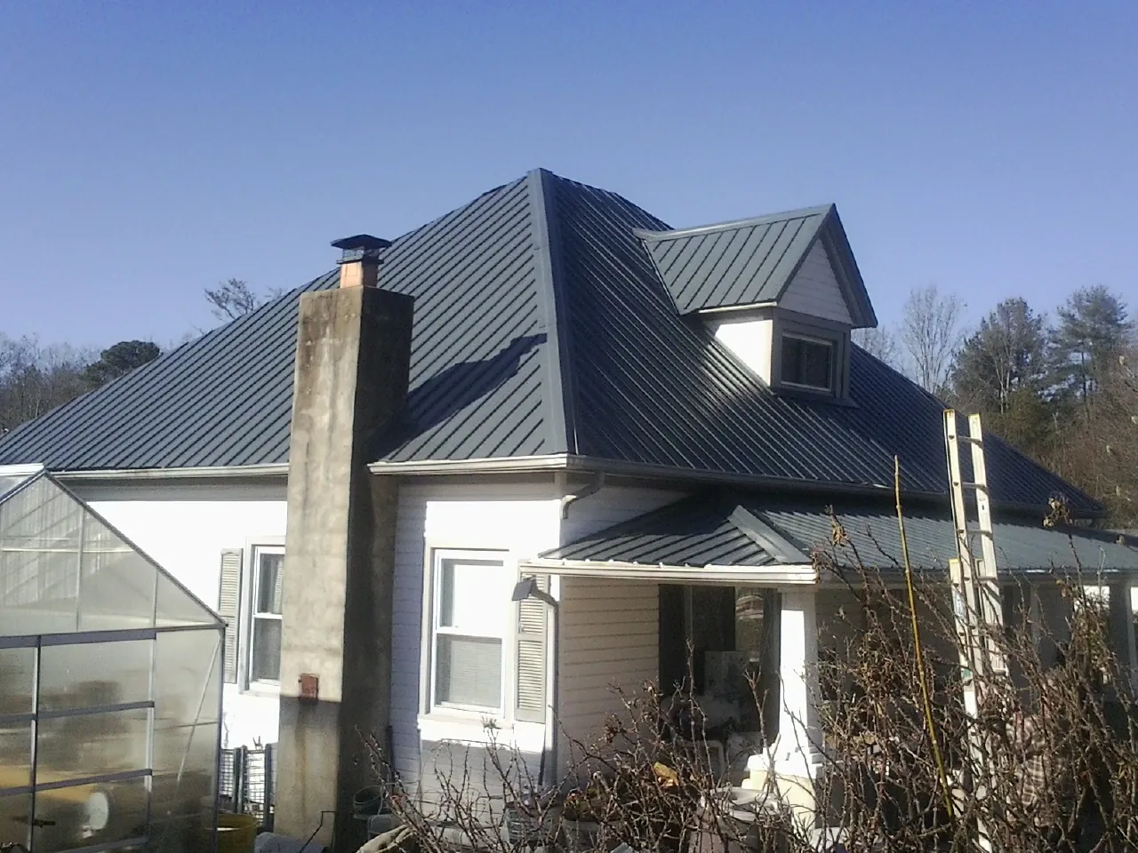 Dark blue standing seam metal roof on a white farmhouse with dormer — Slate & Tile Roof Repair by Roofing Brothers in Enterprise