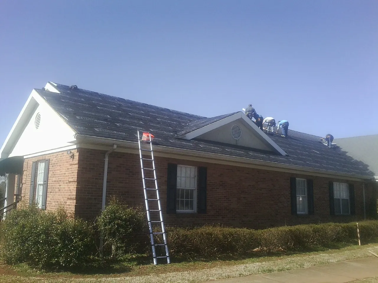 Crew tearing shingles off a brick ranch roof with a ladder set — Emergency Roof Repair work by our crew in Enterprise